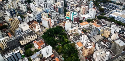 Florianópolis terá oficinas para ouvir moradores sobre problemas no trânsito e transporte Vista aérea do Centro de Florianópolis, com prédios, ruas e áreas arborizadas, ilustrando os desafios do trânsito e transporte na Capital e a discussão sobre mobilidade urbana.