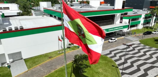 Orçamento de SC prevê R$ 62,9 bilhões para 2027 e crescimento de 8,6% nas receitas Bandeira de Santa Catarina em frente ao Centro Administrativo do Governo do Estado, imagem que ilustra a proposta do orçamento de SC para 2027.