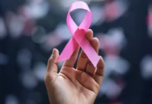 Mão segura laço rosa, símbolo do Outubro Rosa, campanha de conscientização sobre a prevenção e o diagnóstico precoce do câncer de mama.