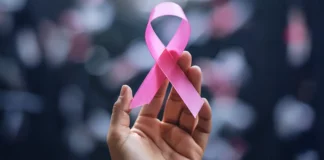 Mão segura laço rosa, símbolo do Outubro Rosa, campanha de conscientização sobre a prevenção e o diagnóstico precoce do câncer de mama.