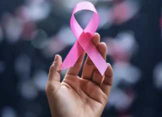 Mão segura laço rosa, símbolo do Outubro Rosa, campanha de conscientização sobre a prevenção e o diagnóstico precoce do câncer de mama.