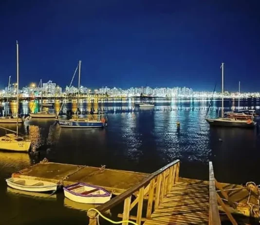 São José recebe 1ª Regata Plínio Verani de Veleiros de Oceano Veleiros ancorados à noite na Baía Sul, com luzes da cidade refletidas na água. Imagem ilustra a 1ª Regata Plínio Verani de Veleiros de Oceano, em São José.