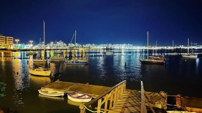 regata-plinio-verani-1200x675 Veleiros ancorados à noite na Baía Sul, com luzes da cidade refletidas na água. Imagem ilustra a 1ª Regata Plínio Verani de Veleiros de Oceano, em São José.