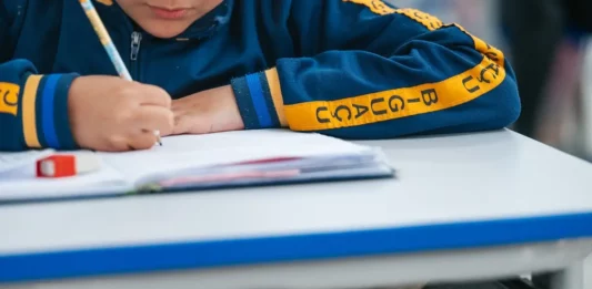 Estudante escreve em caderno durante atividade escolar; imagem ilustra o calendário de rematrículas e matrículas da Rede Municipal de Biguaçu para 2027.