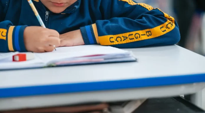 Estudante escreve em caderno durante atividade escolar; imagem ilustra o calendário de rematrículas e matrículas da Rede Municipal de Biguaçu para 2027.