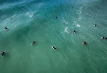 Florianópolis abre 307 vagas para atividades nas praias durante o verão Vista aérea de surfistas no mar, ilustrando as autorizações para aulas de surfe e outras atividades nas praias de Florianópolis durante o verão 2026/2027.