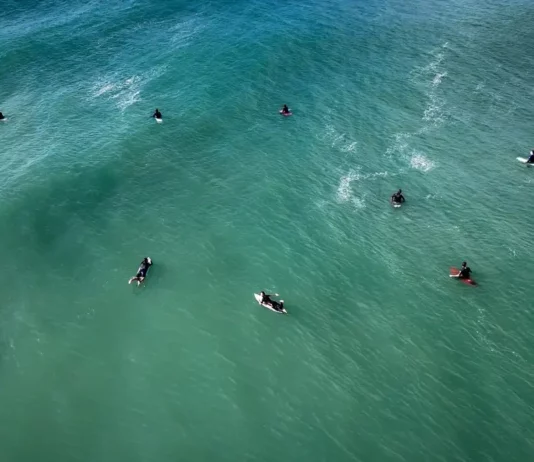 Florianópolis abre 307 vagas para atividades nas praias durante o verão Vista aérea de surfistas no mar, ilustrando as autorizações para aulas de surfe e outras atividades nas praias de Florianópolis durante o verão 2026/2027.