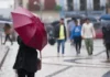 Santa Catarina tem alerta de temporais e chuva intensa nesta sexta-feira; veja regiões de maior risco Pessoa segura guarda-chuva vermelho enquanto pedestres caminham sob chuva em uma área urbana de Santa Catarina.